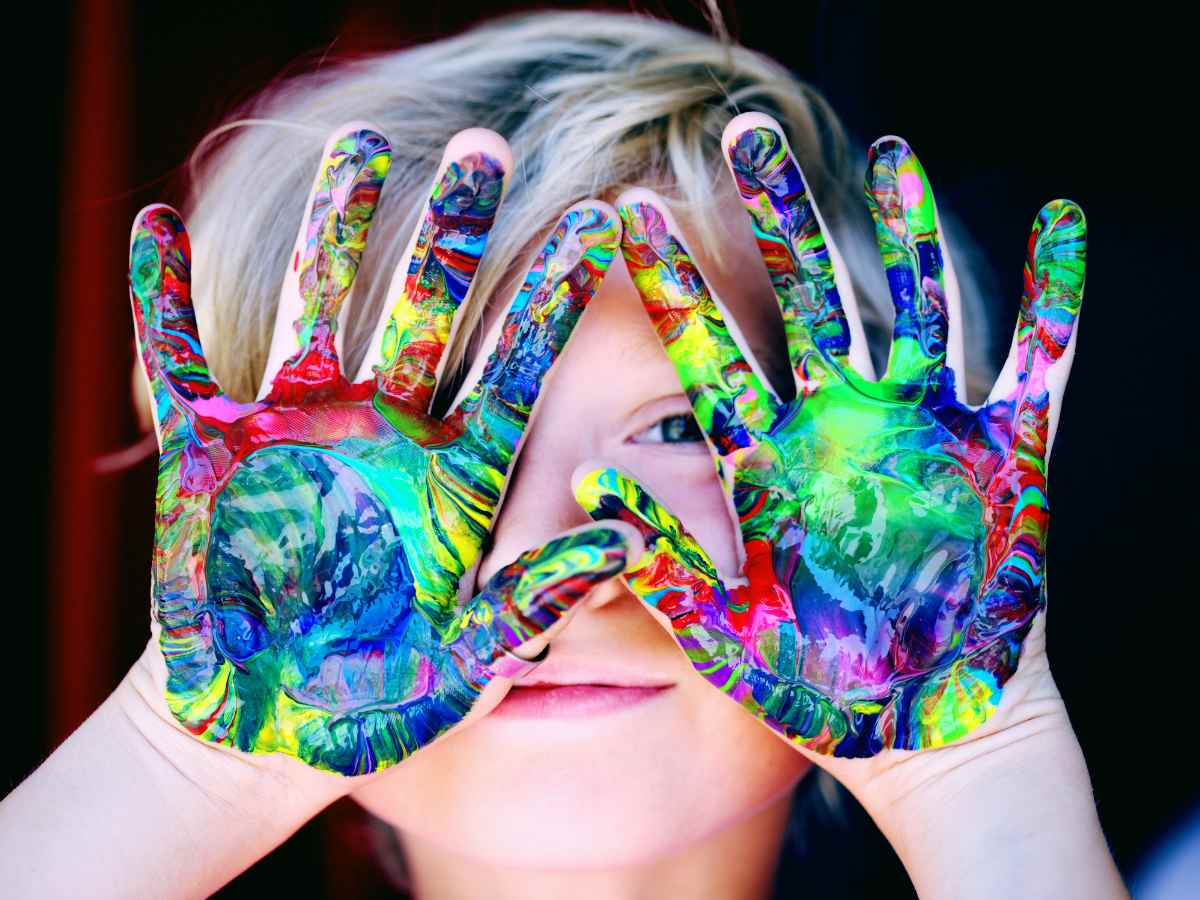 Kid holding hands up in front of face. Hands have different colors of paint all over them for article School Districts in Dallas-Fort Worth, TX for newcomers moving to DFW area.