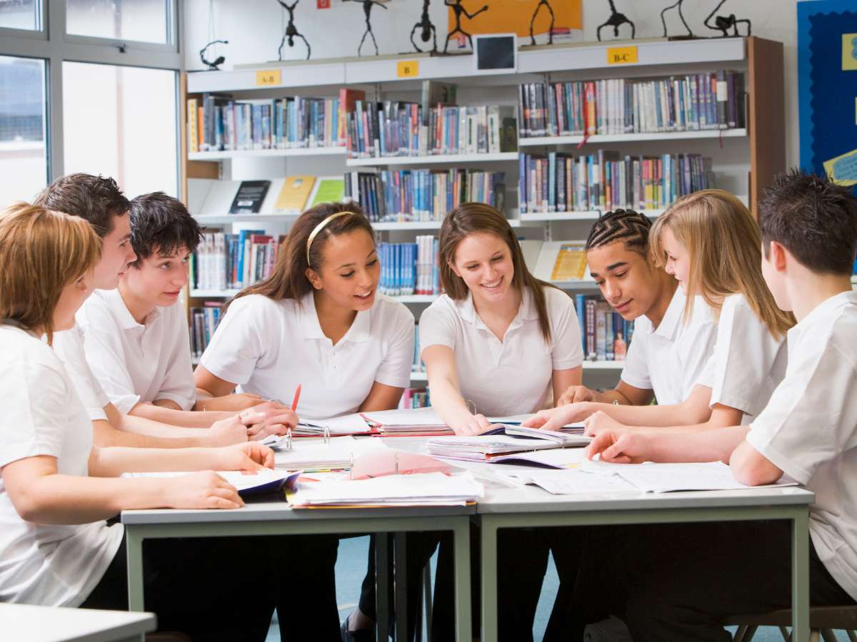 Group of 8 private school kids working at a table together in a room with shelves of books behind them for article Top 20 Private Schools in DFW for newcomers moving to DFW.