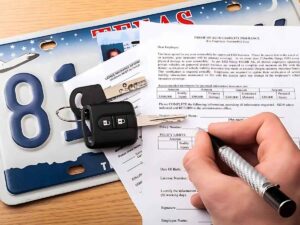 Texas plate with license, insurances forms and keys on top with hand filling out forms for article Moving to Texas with a Car: Avoid Fines with These 6 Must-Know Tips for newcomers moving to DFW.