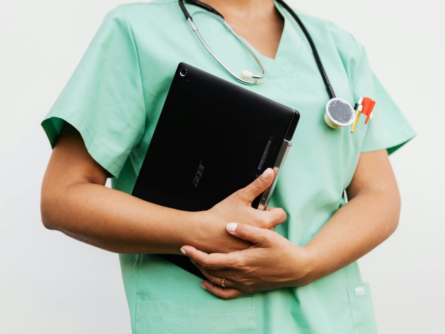 person wearing mint green scrubs holding a laptop, wearing a stethescope