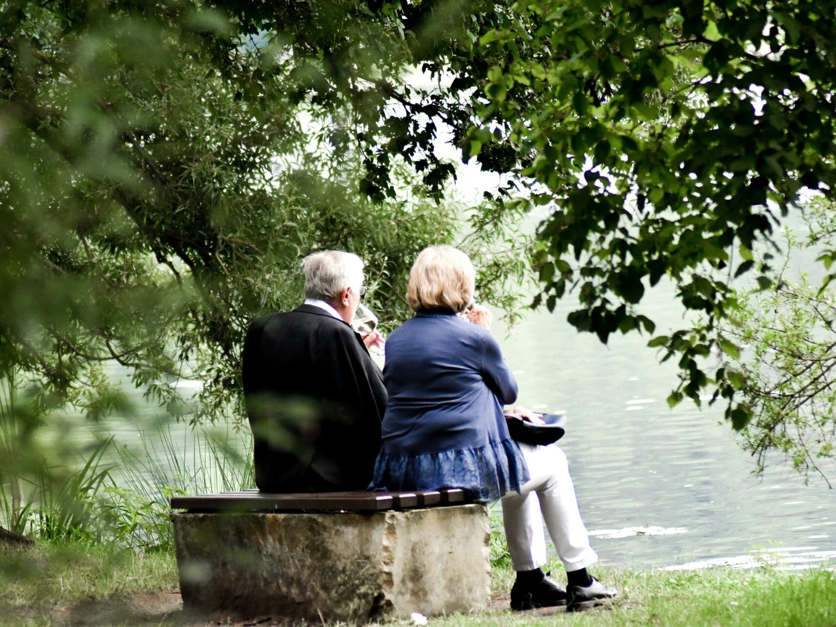 older couple sitting on bench facing towards the lake