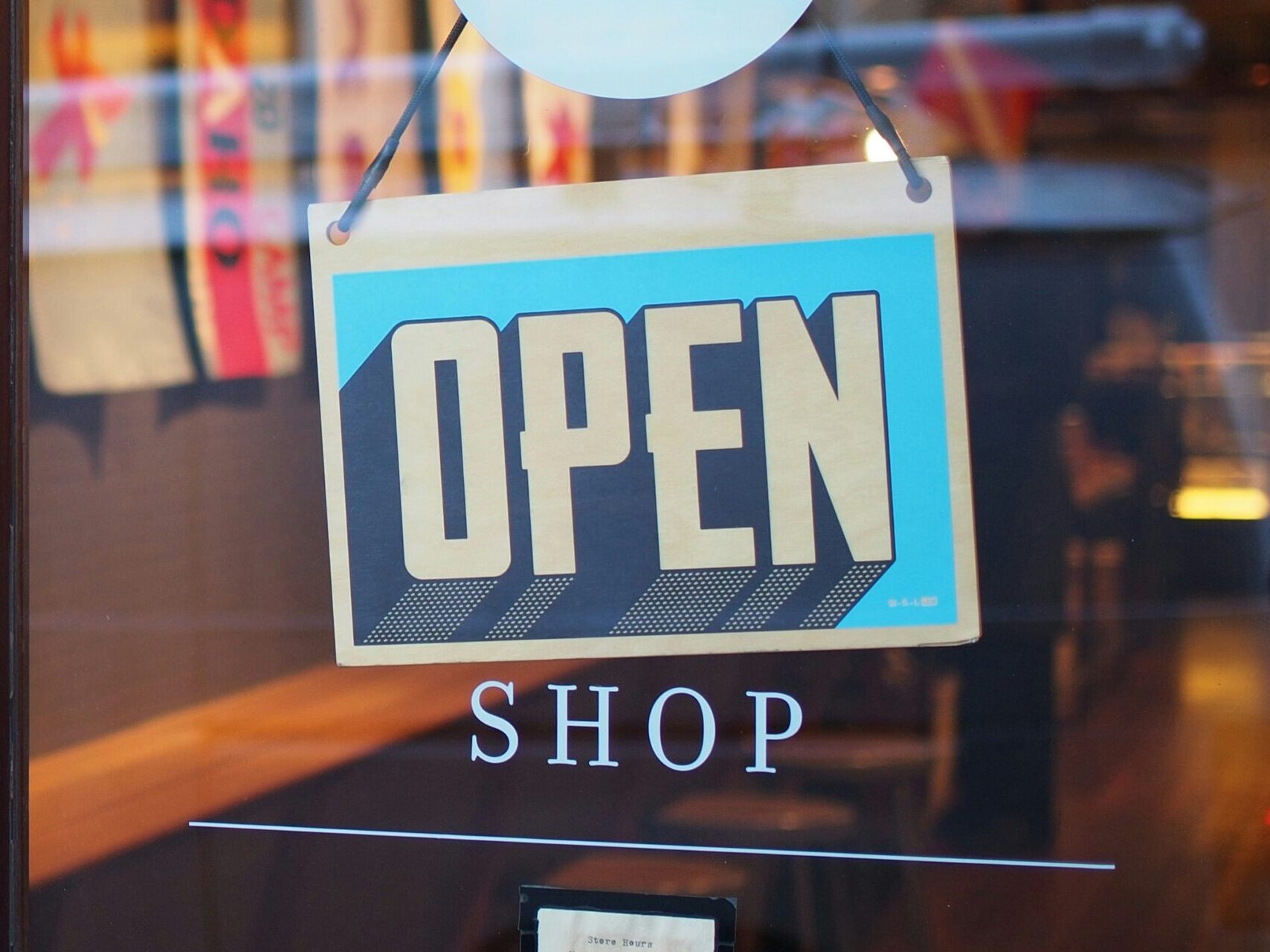"OPEN" sign showing on clear business door with the word "shop" underneath