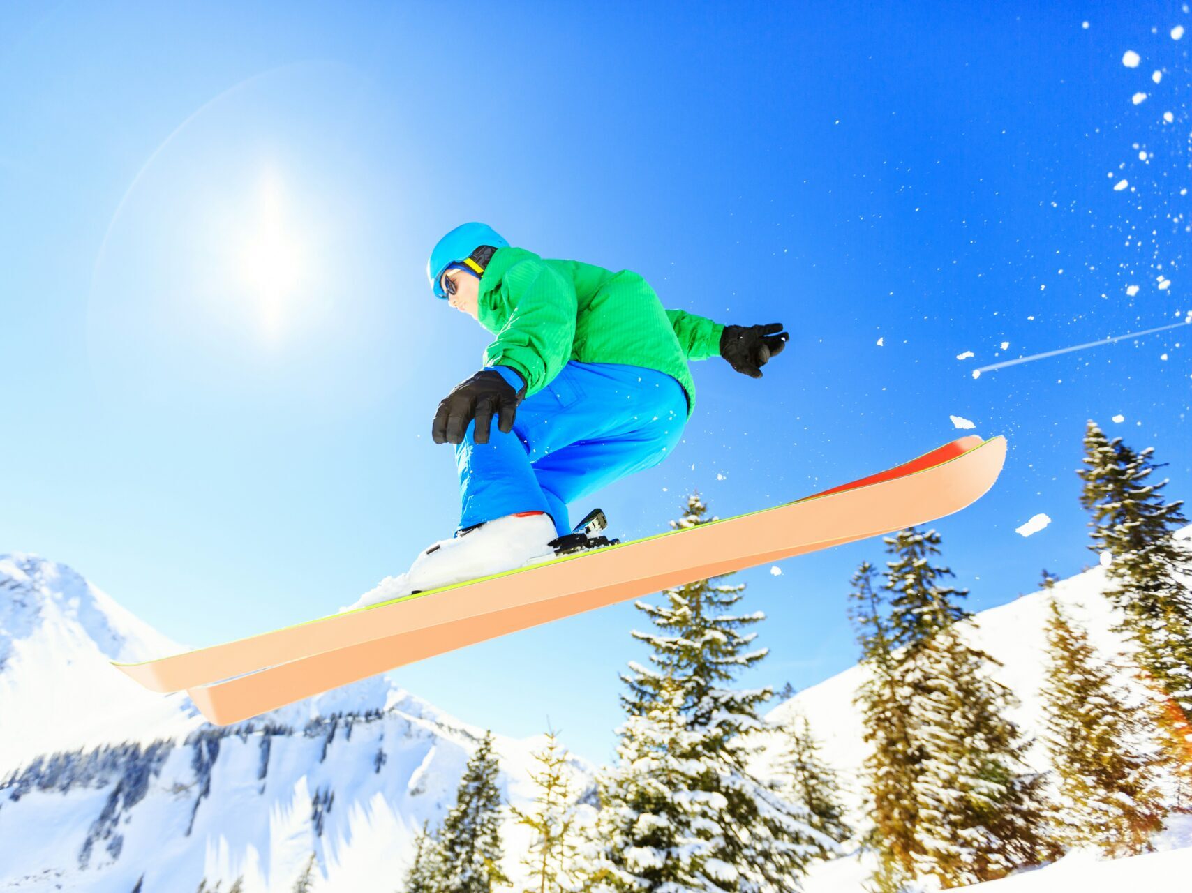 person wearing green jacket, blue ski pants and helmet making a jump wearing snow skis