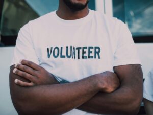 man with arms crossed wearing a white t-shirt with the word "volunteer" on it