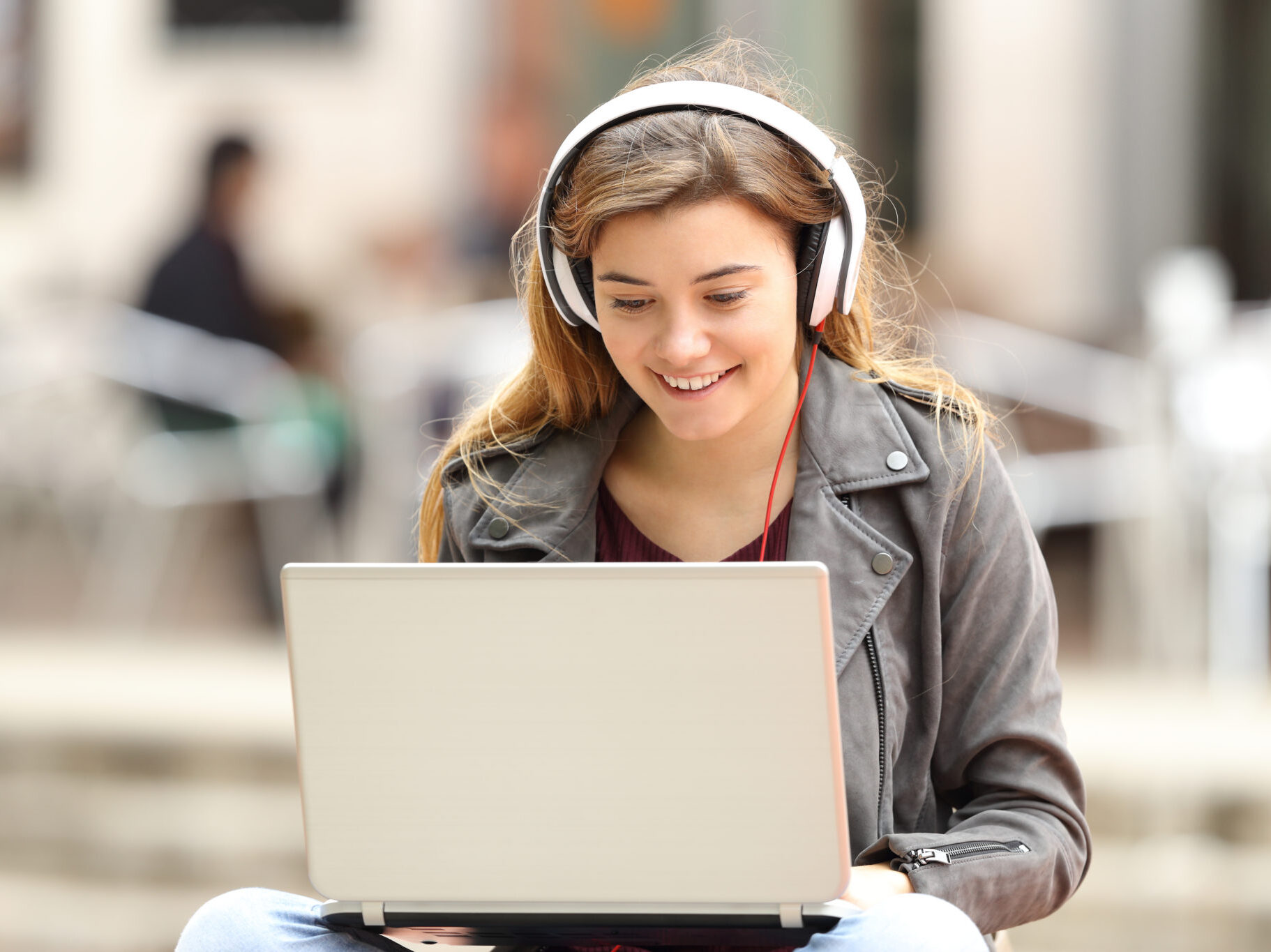 female student sitting outside on laptop with headphones, smiling