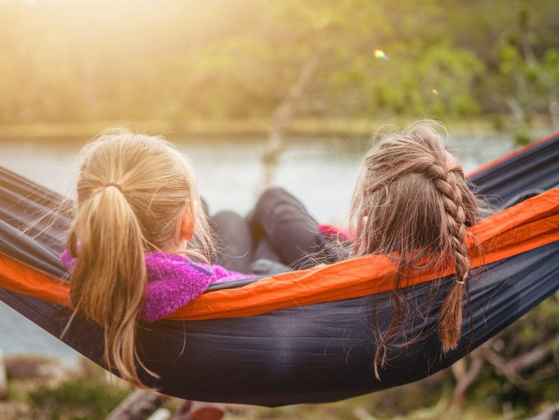 2 young girls laying in a hammock facing a lake or river