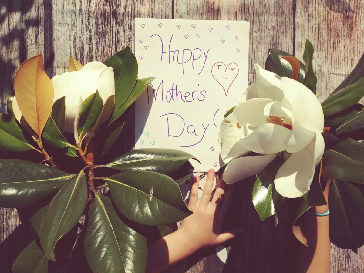 handwritten sign with "Happy Mother's Day" posted on a fence with flowers in foreground