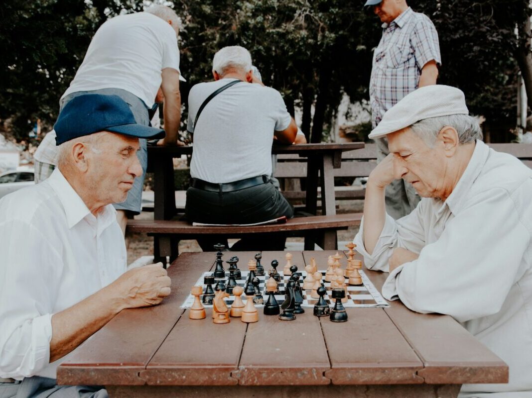 two older gentlemen playing chess outside on a picnic table