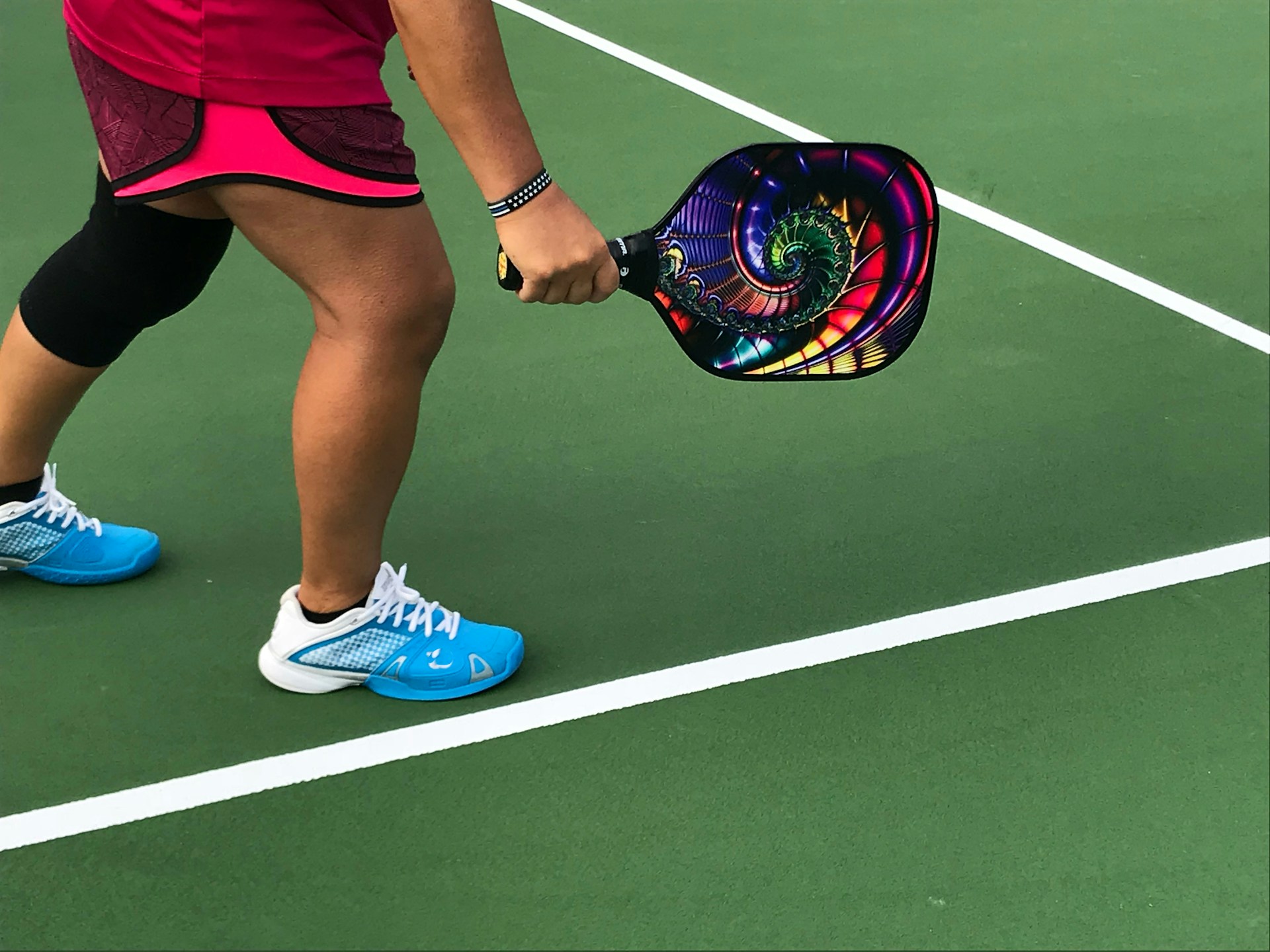 athlete in ready position holding a colorful pickleball racket on a court in the daytime