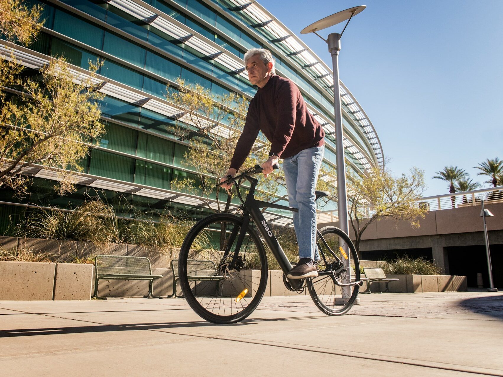 man in red long sleeve shirt and pants riding a bicycle in the daytime in front of a glass building