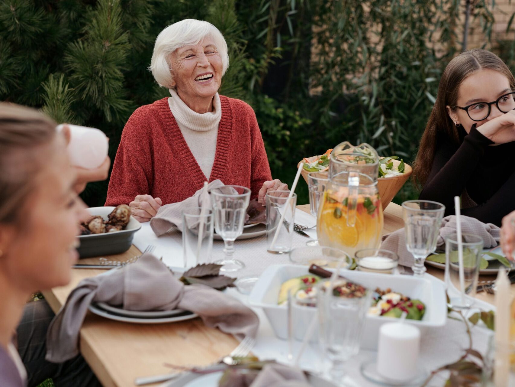 Older woman at the head of a table, smiling, having a meal with group outside