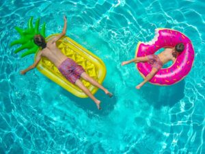 2 boys floating on colorful pool floaties in bright aqua swimming pool