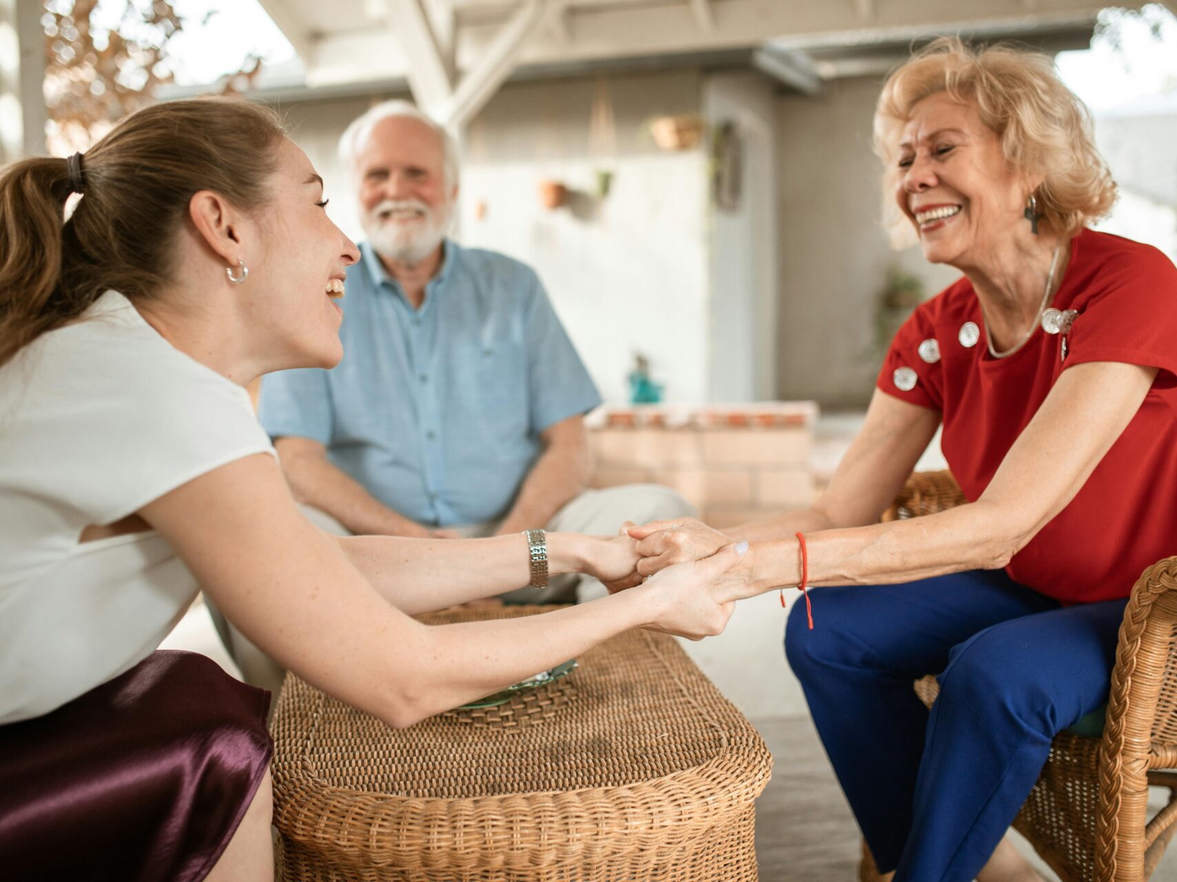 older woman holding the hands of a younger woman, smiling with older man in the background smiling