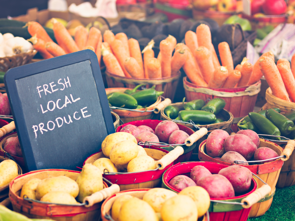 Tables with fresh produce at a Farmers Market with a chalkboard sign on the table that says fresh local produce.