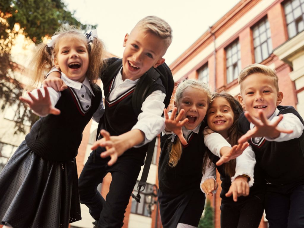 5 kids in school uniforms reaching toward camera.