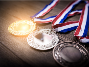 1st, 2nd, 3rd place medals stacked on table with red, white and blue ribbons attached.