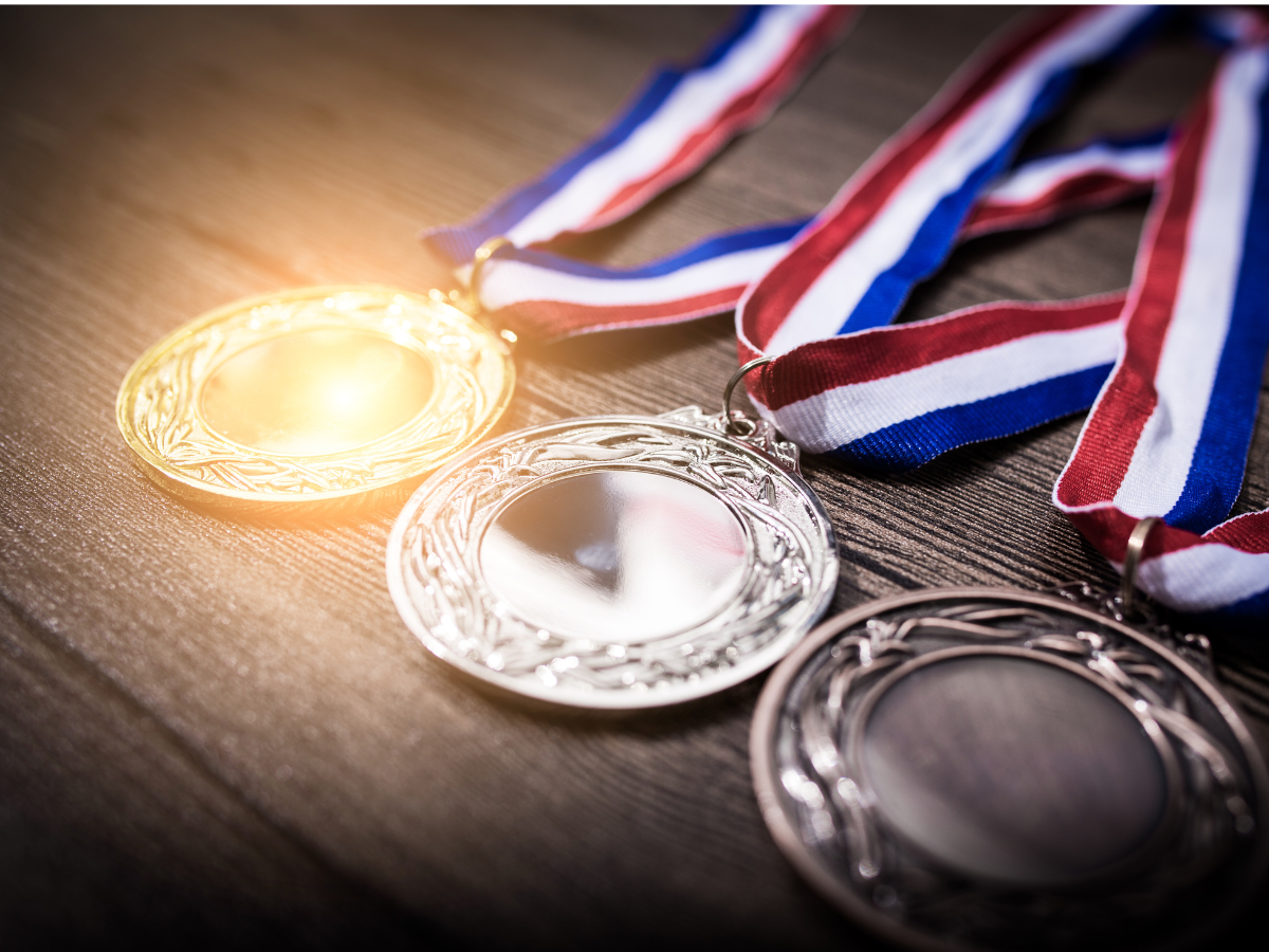 1st, 2nd, 3rd place medals stacked on table with red, white and blue ribbons attached.