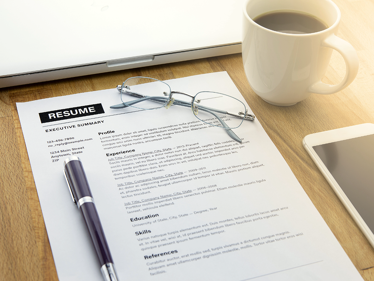 Desk with coffee, phone, glasses, pen on resume.