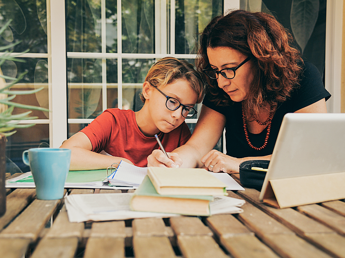 Mom homeschooling son at table with laptop and papers on it.