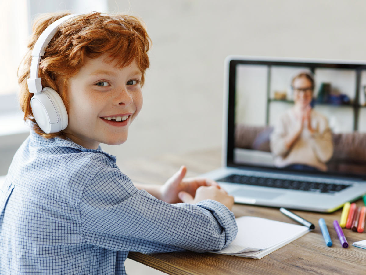 A boy with headphones on learning from an online tutor.