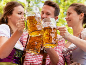 3 people dressed in costume at oktoberfest cheering large clear beer steins full of beer.