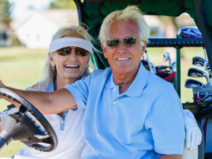 Senior couple sitting in golf cart smiling at camera.