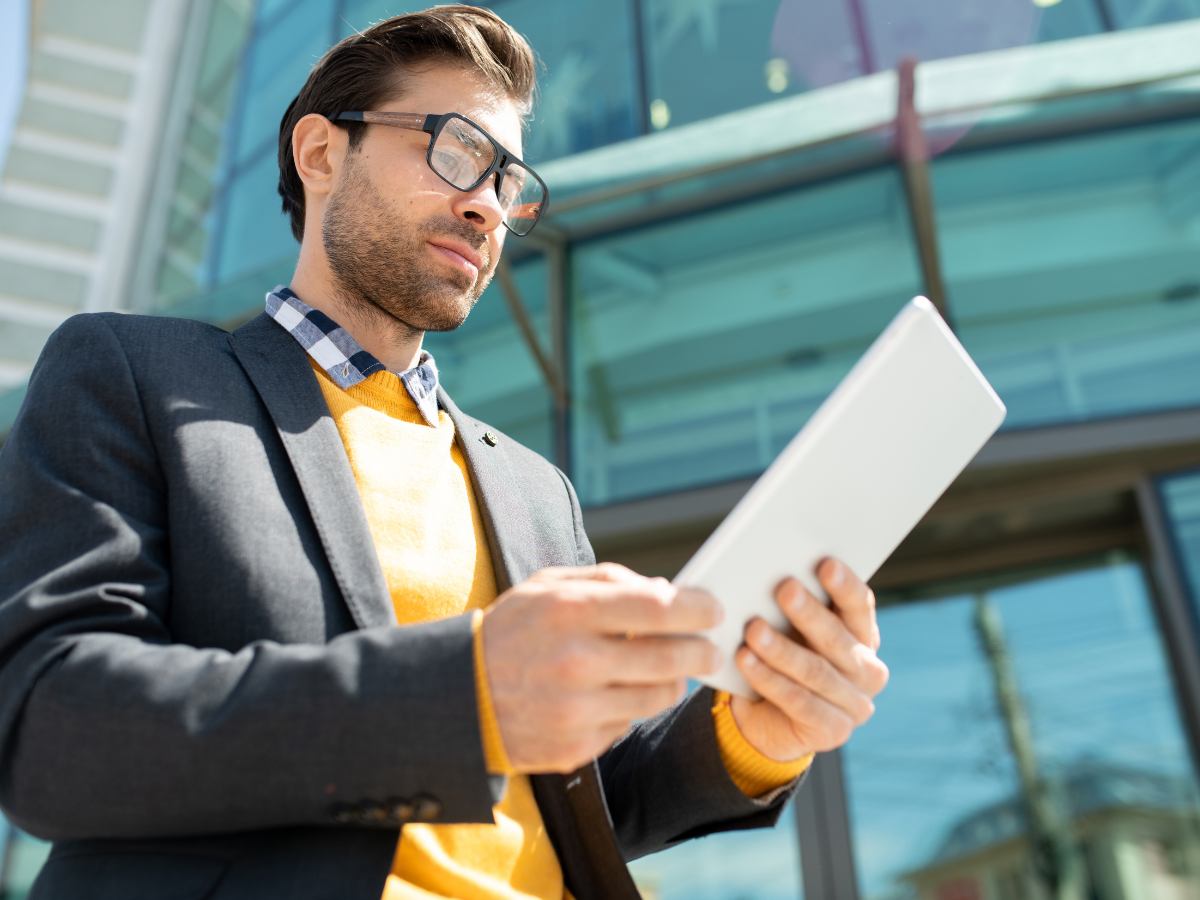 Man in suit looking at tablet in front of building for article Employment in DFW: Critical Resources for Job Seekers for newcomers moving to DFW.