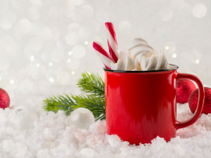 Red coffee mug with whip cream and candy canes coming out the top on a bed of white sparkly snow with pine and red balls in the background for article The 12 Best Coffee Shops in DFW for Newcomers moving to DFW.