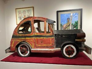 Gallery with car on platform with red carpet and 2 paintings behind it at the African American Museum in Dallas for article Exploring African American Heritage in DFW for newcomers moving to DFW.