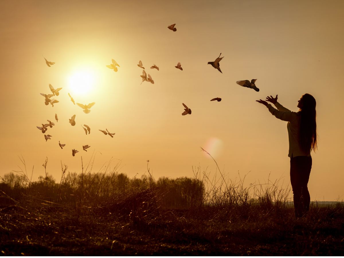 Woman at sunrise with arms outstretched to the sky releasing birds of peace for article Faith and Worship in Dallas-Fort Worth for newcomers moving to DFW area.