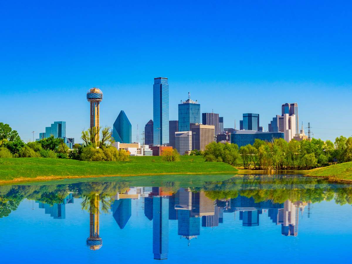 Dallas downtown skyline bright blue sky and with lake in foreground reflecting the skyline for article Why Move to Dallas Texas for newcomers moving to DFW.