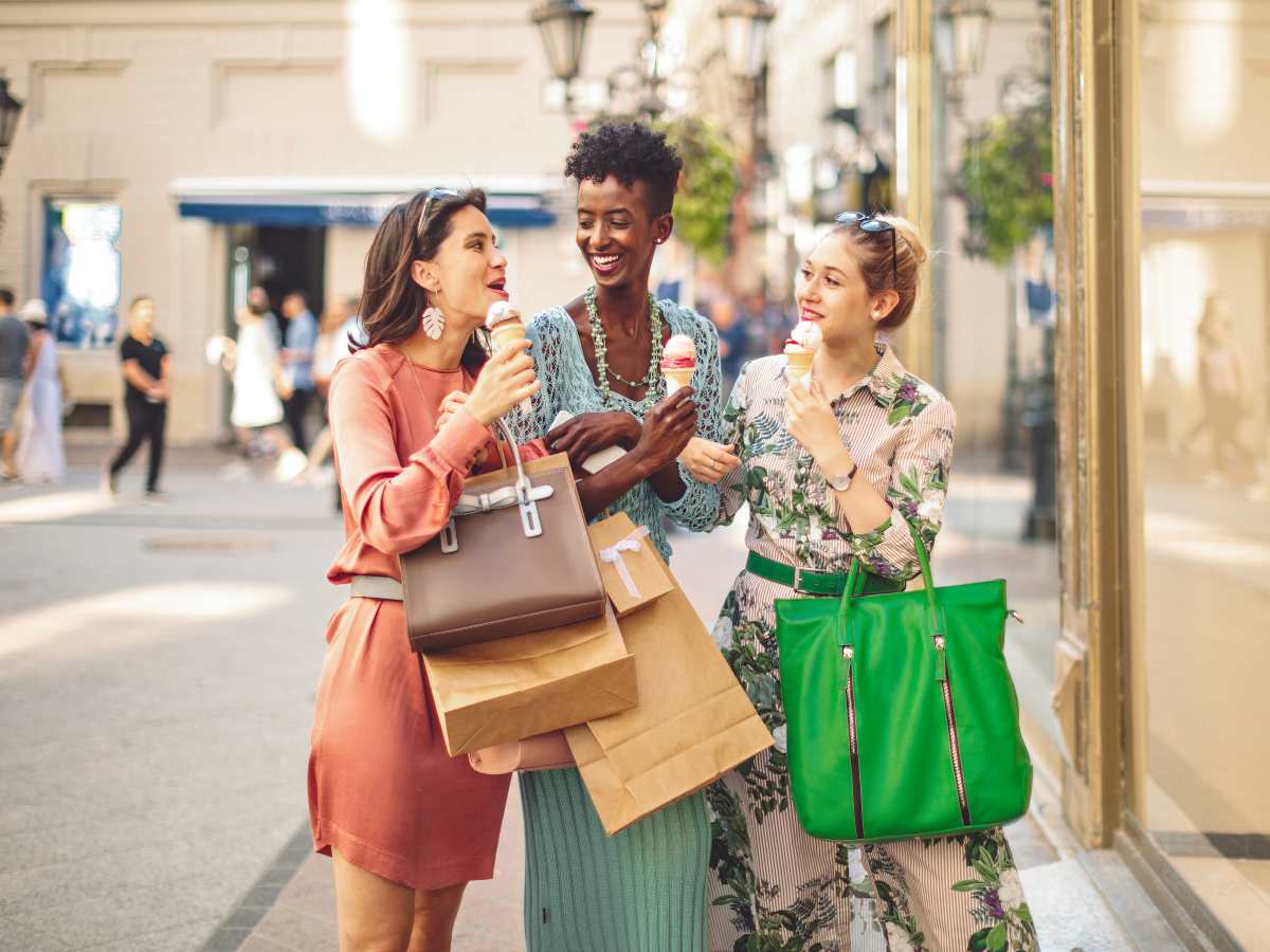 3 women smiling, laughing, and walking down street with shopping bags and ice cream cones in hand for article The Best Shopping and Dining in DFW for newcomers moving to DFW.