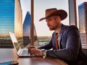 A Person in a Cowboy Hat and business suit sitting at desk in office skyscraper in Dallas for article DFW Myths vs Reality for newcomers moving to DFW.