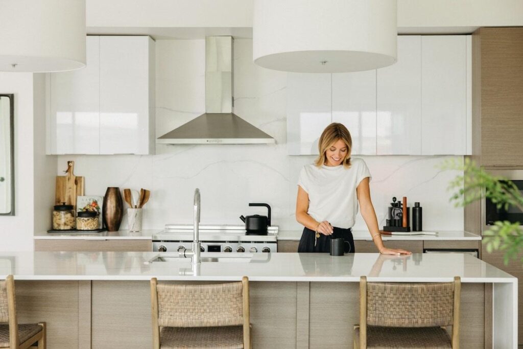 Woman behind large white kitchen counter in modern kitchen at One Ranger Way for article The Best Place to Live in DFW Might Be Exactly Between Dallas and Fort Worth for newcomers moving to DFW area.