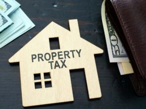 wallet with money and a wood cutout of a house that says property taxes for article How to Save on Property Taxes in Texas