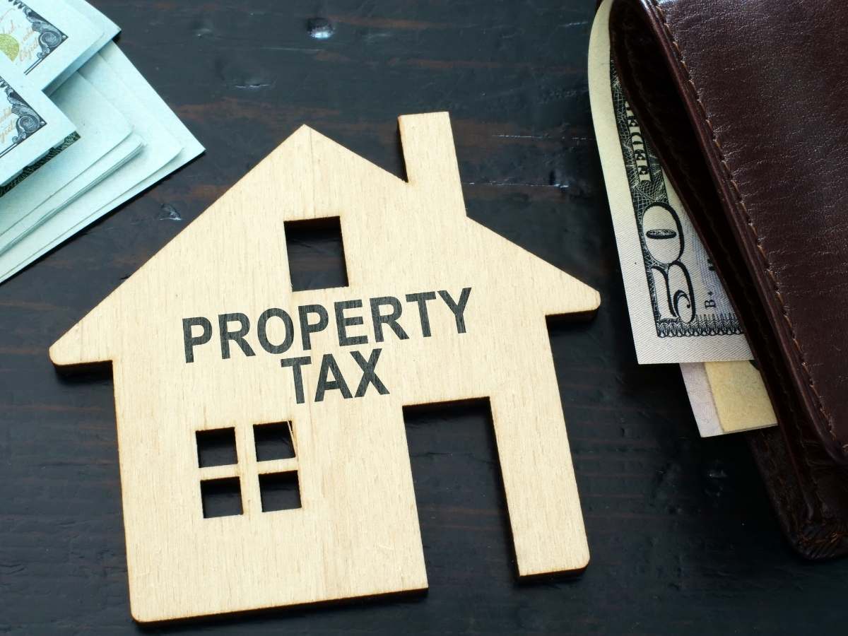 wallet with money and a wood cutout of a house that says property taxes for article How to Save on Property Taxes in Texas