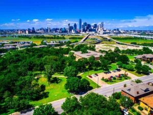 Aerial view - Dallas skyline in background with trees, houses, and green spaces in foreground for article DFW Housing Market 2025: What Buyers and Renters Need to Know