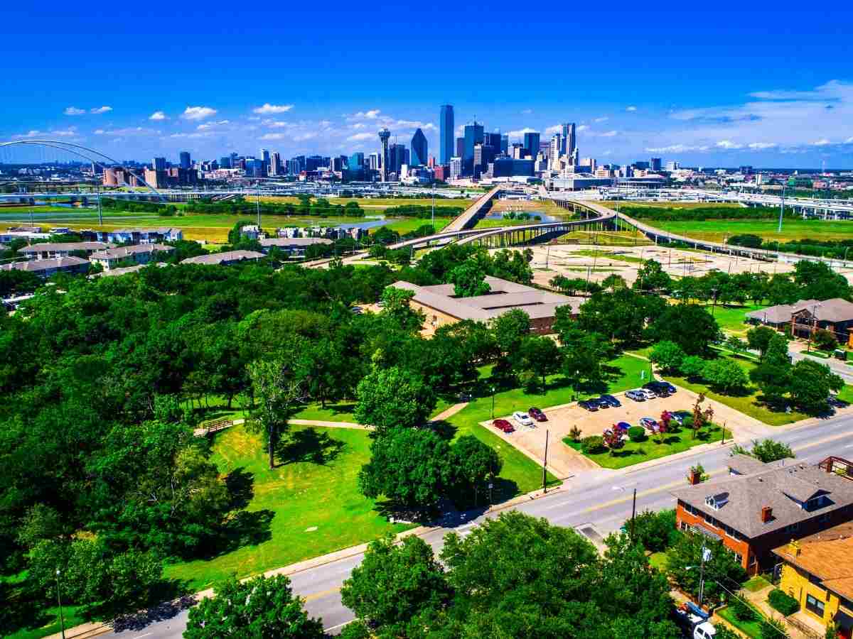 Aerial view - Dallas skyline in background with trees, houses, and green spaces in foreground for article DFW Housing Market 2025: What Buyers and Renters Need to Know